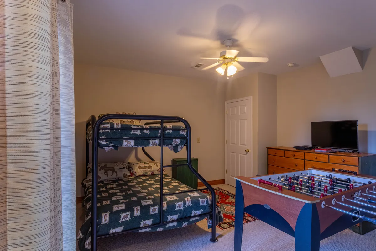 A lively bunk room with a twin-over-full bunk bed, a foosball table ready for games, a wooden dresser, and a TV. The layout is both playful and practical, offering the perfect hangout for kids or teens.