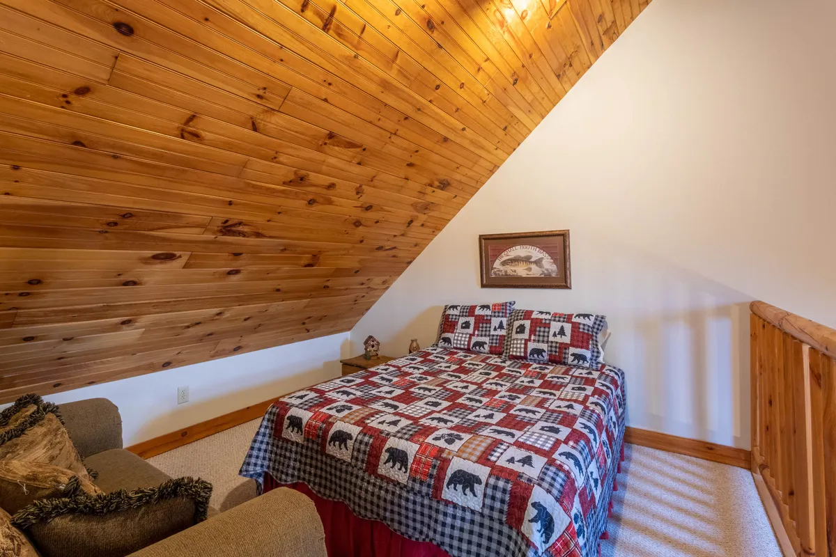 This image showcases a cozy living area with a wooden ceiling, a bed adorned with a patterned quilt, and a sofa positioned by the window. The natural light streaming in hints at the beauty of the surrounding landscape and invites the outdoors in, creating an inviting atmosphere for relaxation after a day of adventure.